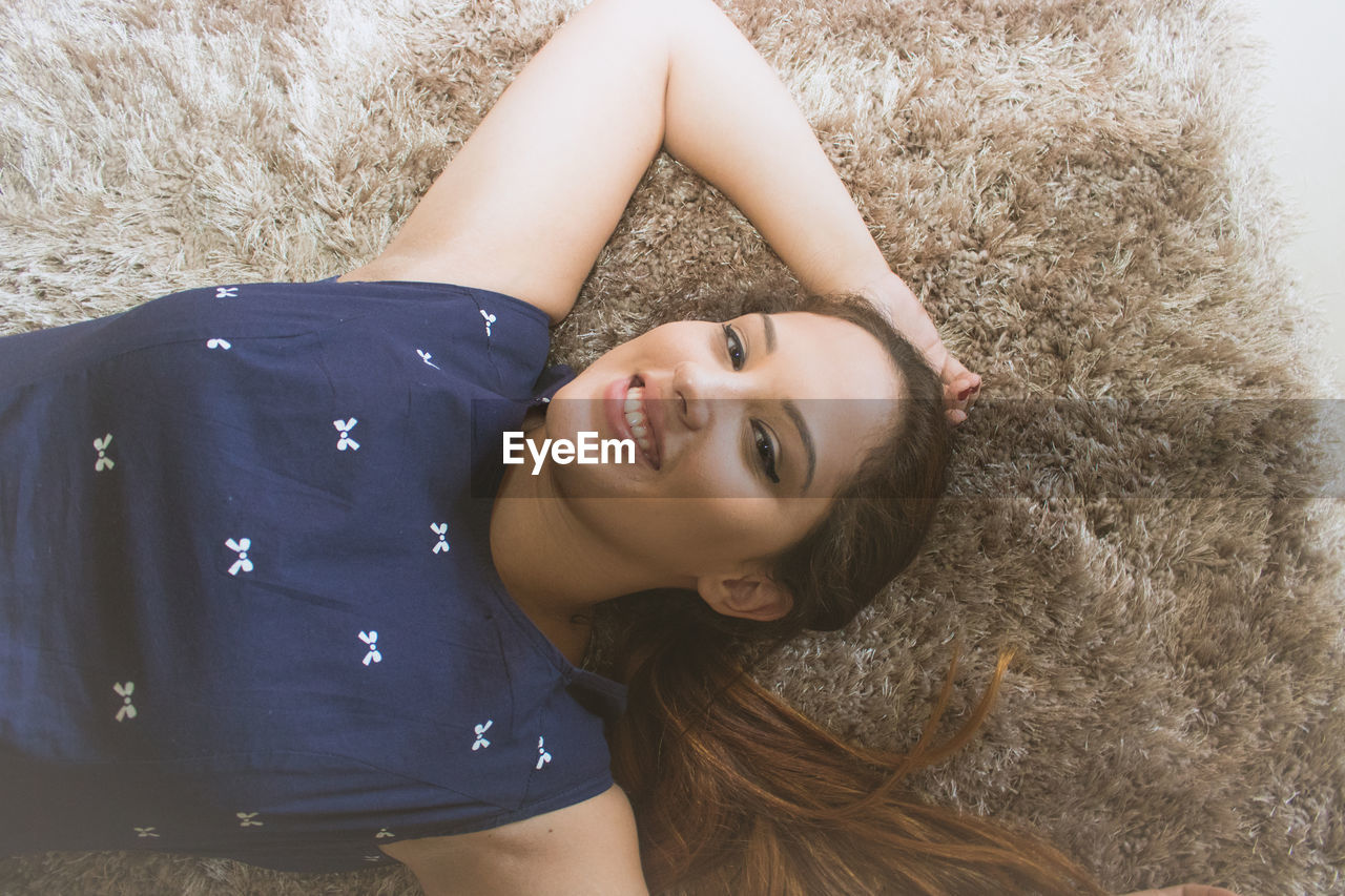 Portrait of smiling young woman lying on area rug