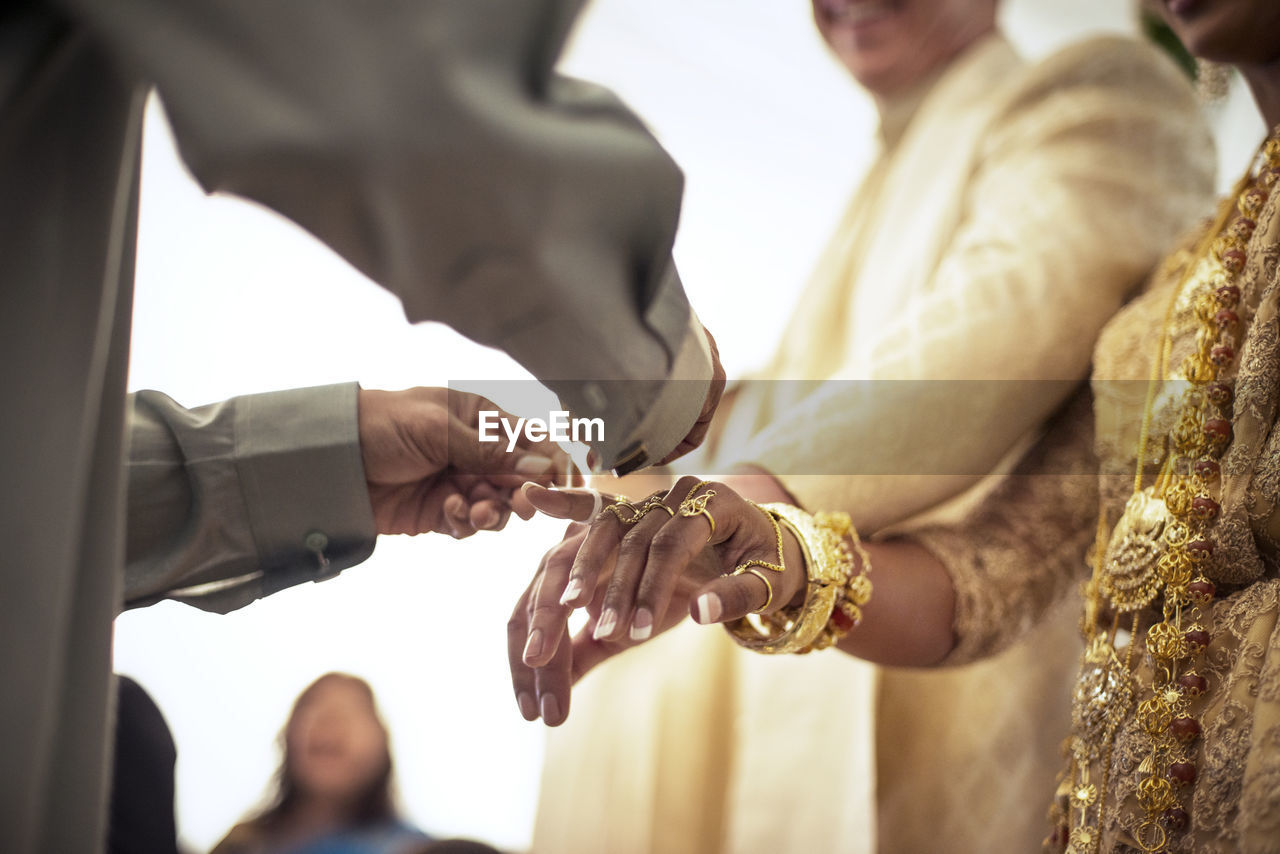 Low angle view of priest tying fingers of bride and groom