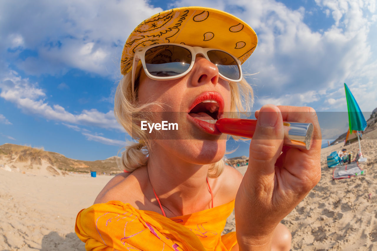 Close-up of mature woman applying lipstick while wearing sunglasses at beach