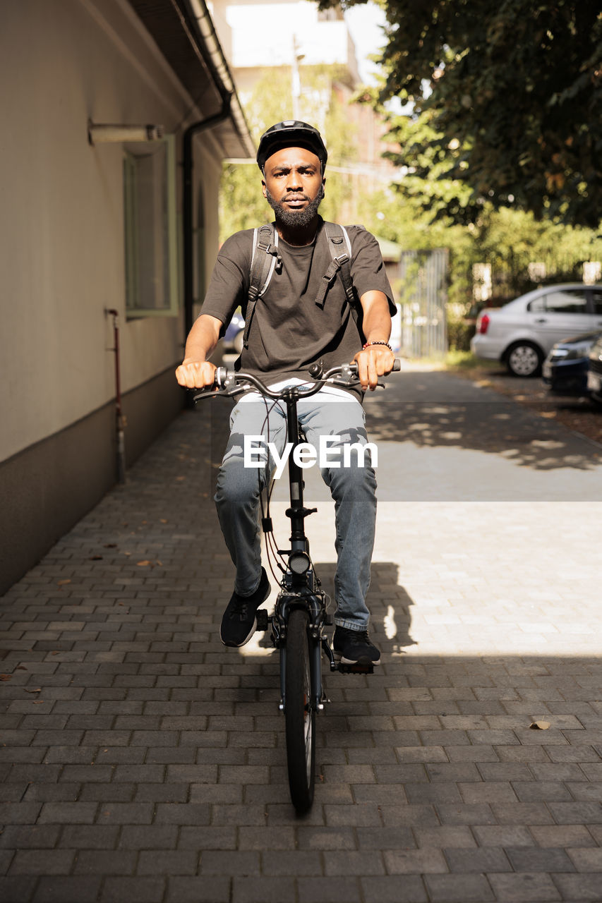 portrait of young man riding bicycle on footpath