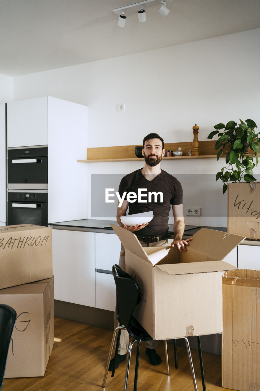 Portrait of man unpacking kitchen utensils from box at new home