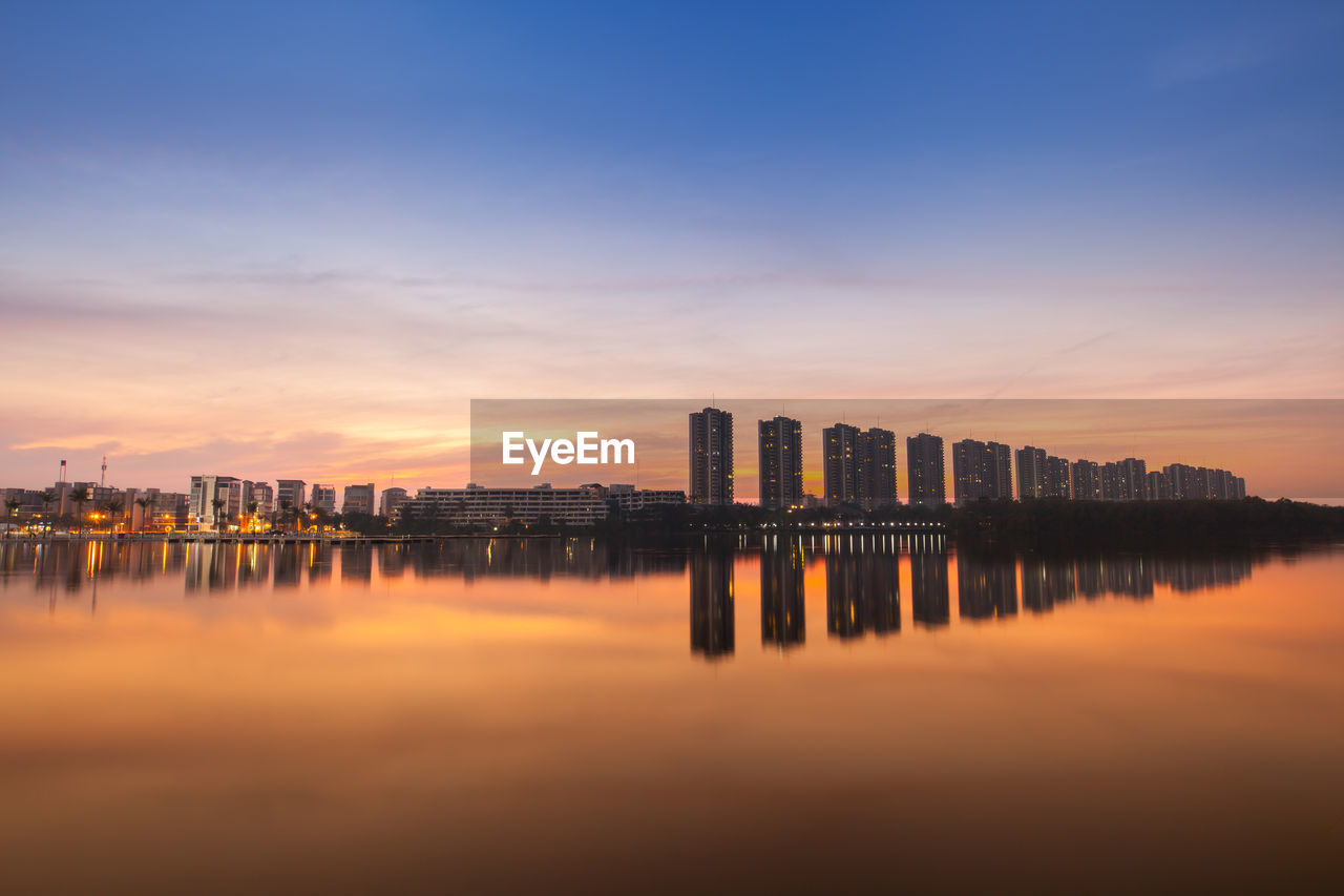 Scenic view of river by buildings against sky during sunset