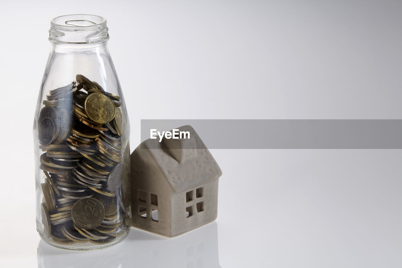 Close-up of model home and coins jar over white background