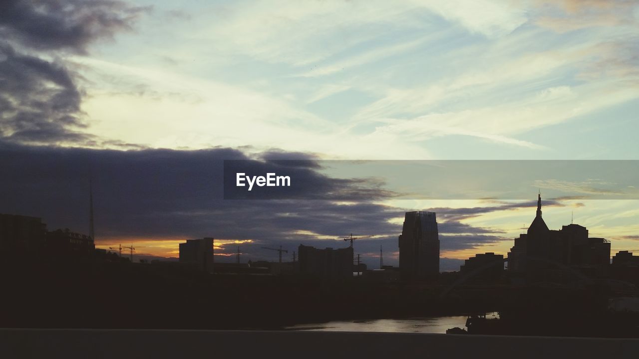 BUILDINGS IN CITY AGAINST CLOUDY SKY AT SUNSET