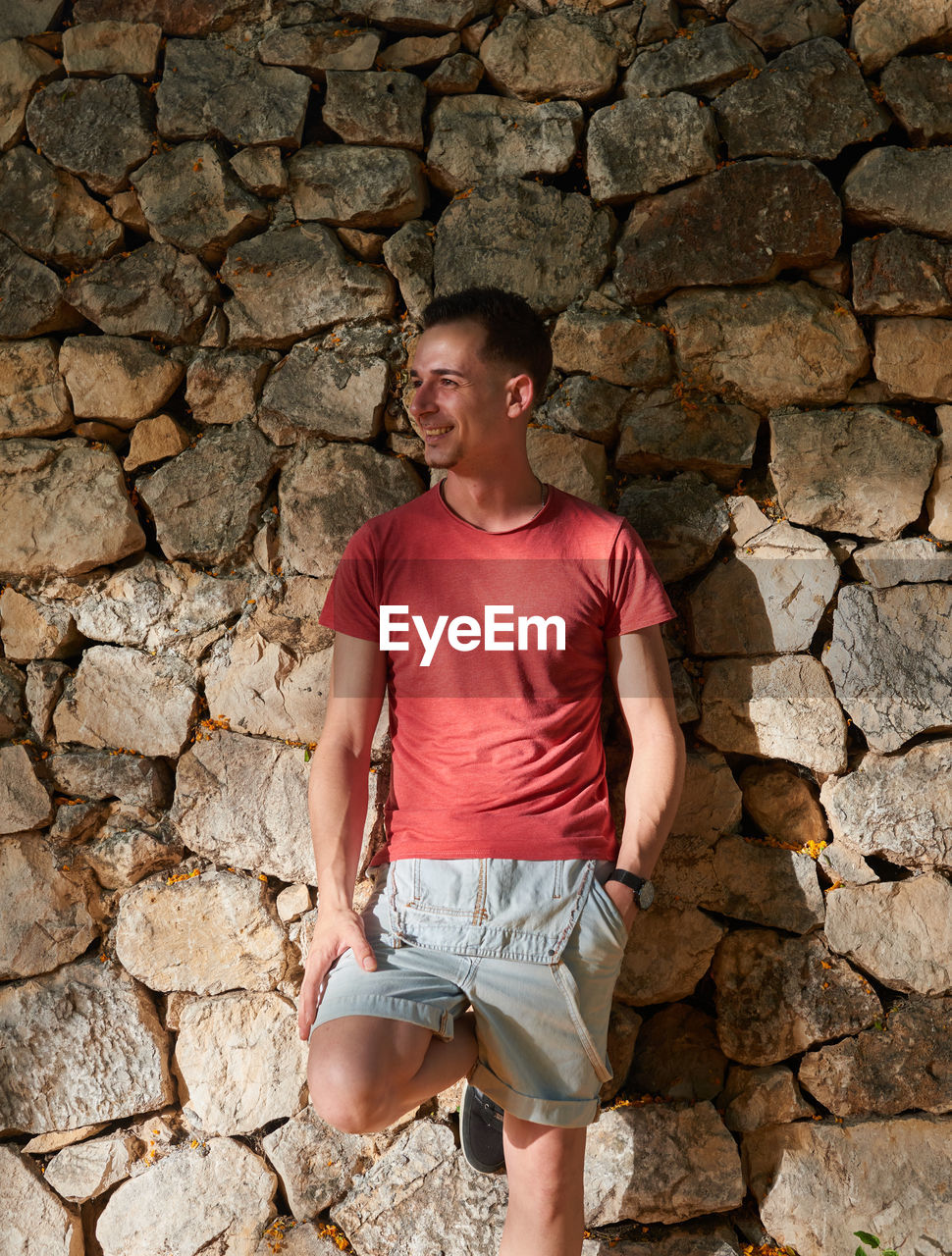 An attractive young man posing on a stone wall.