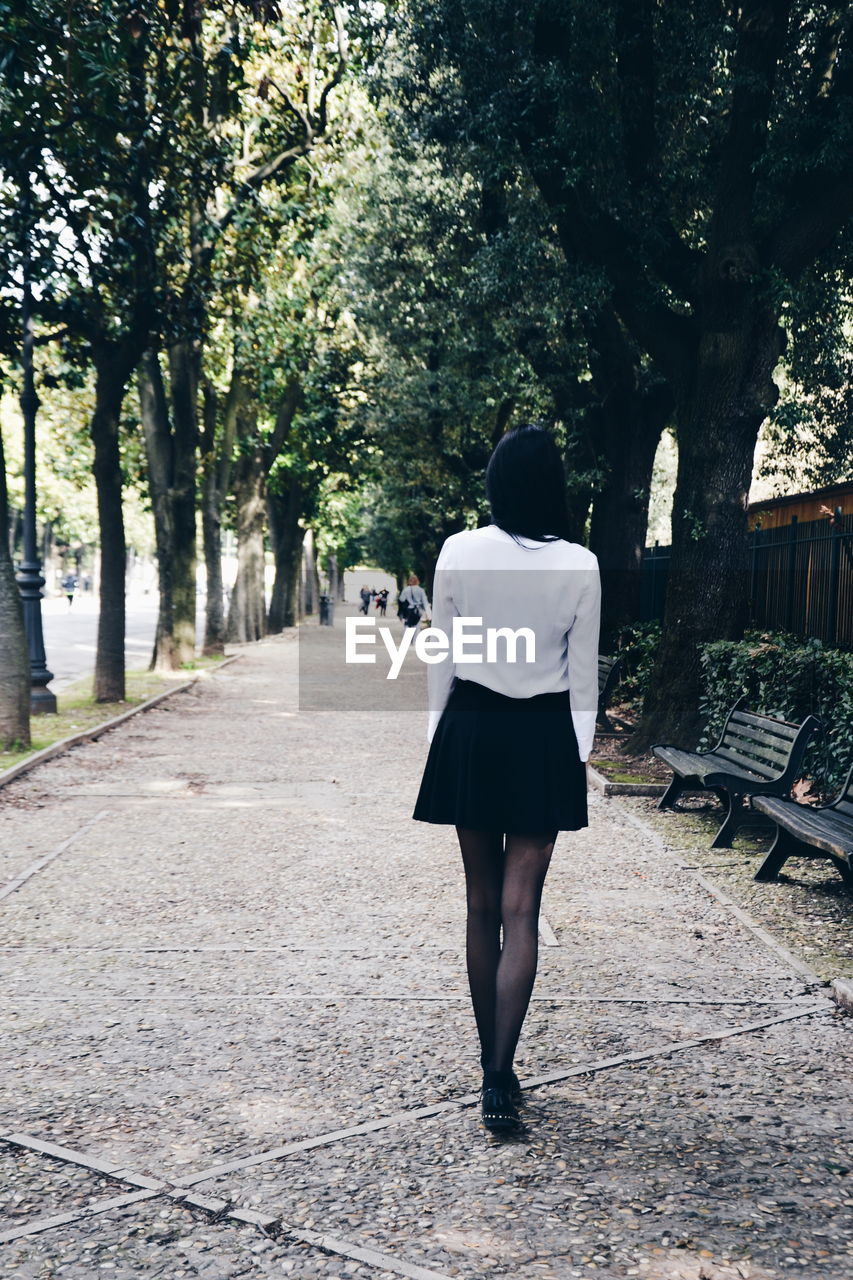 Rear view of woman walking on footpath amidst trees