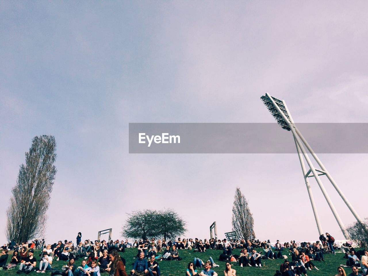 People on grassy field against sky at mauerpark