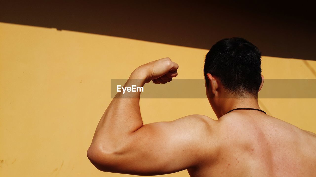 REAR VIEW OF SHIRTLESS MAN AGAINST WALL