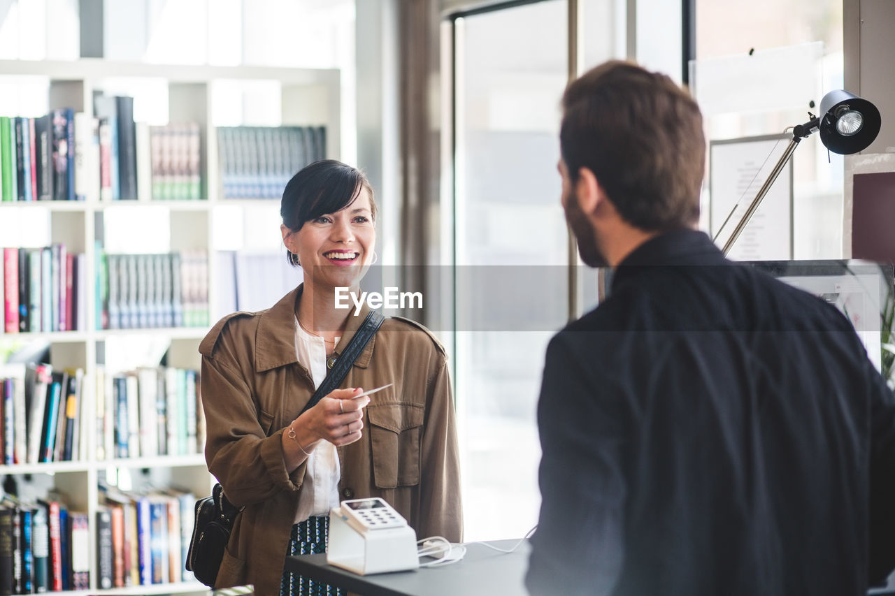 Businesswoman smiling while receiving card to male entrepreneur at counter in office