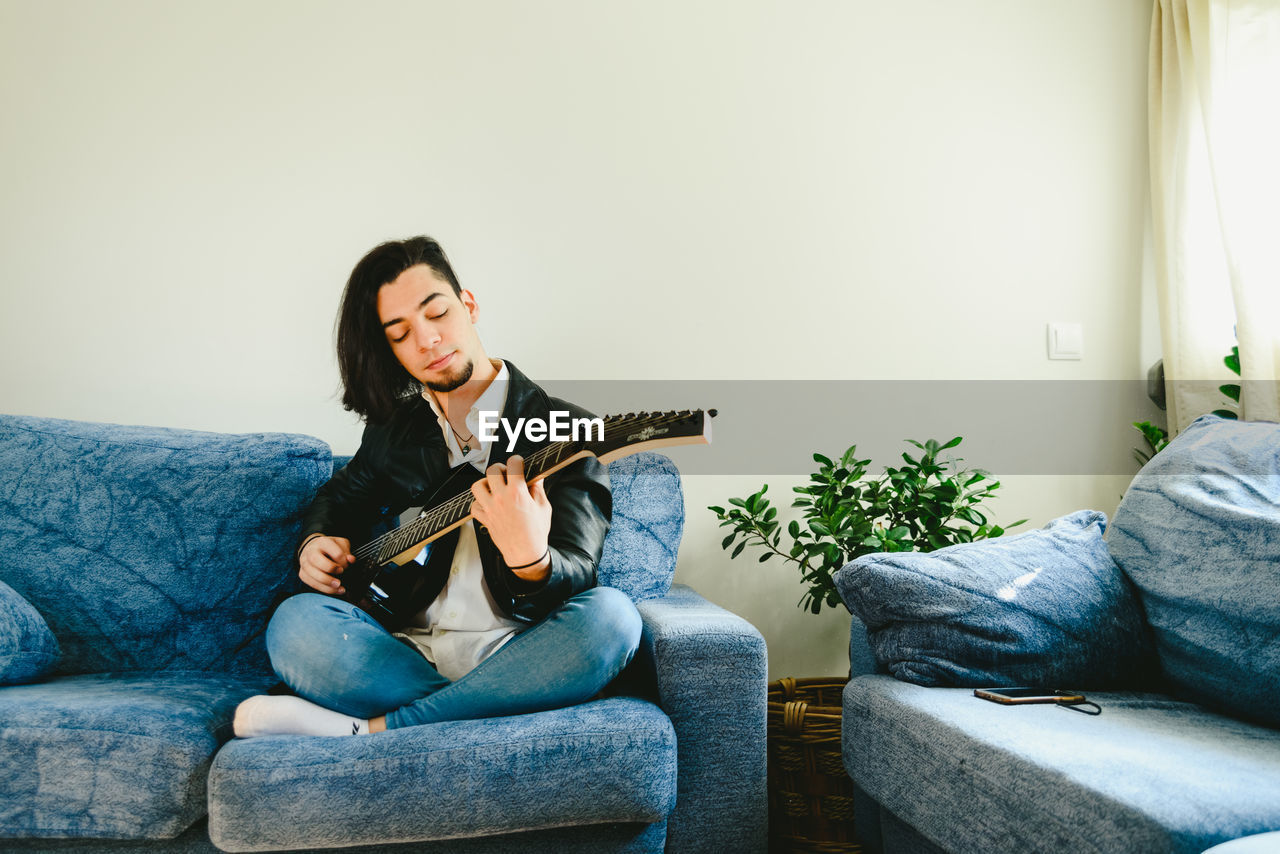 Man playing guitar while sitting on sofa