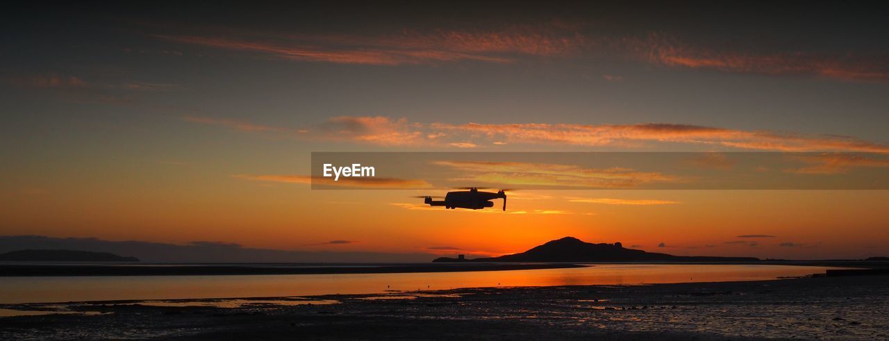 Silhouette drone on beach against sky during sunset