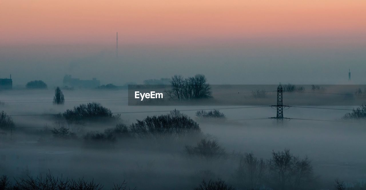 Scenic view of trees in foggy weather against sky during sunset