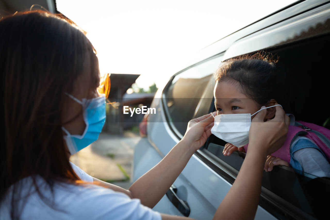 Close-up of mother wearing flu mask to girl in car