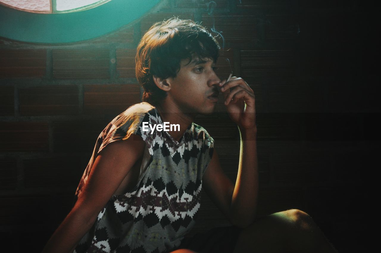 Young man smoking cigarette by brick wall