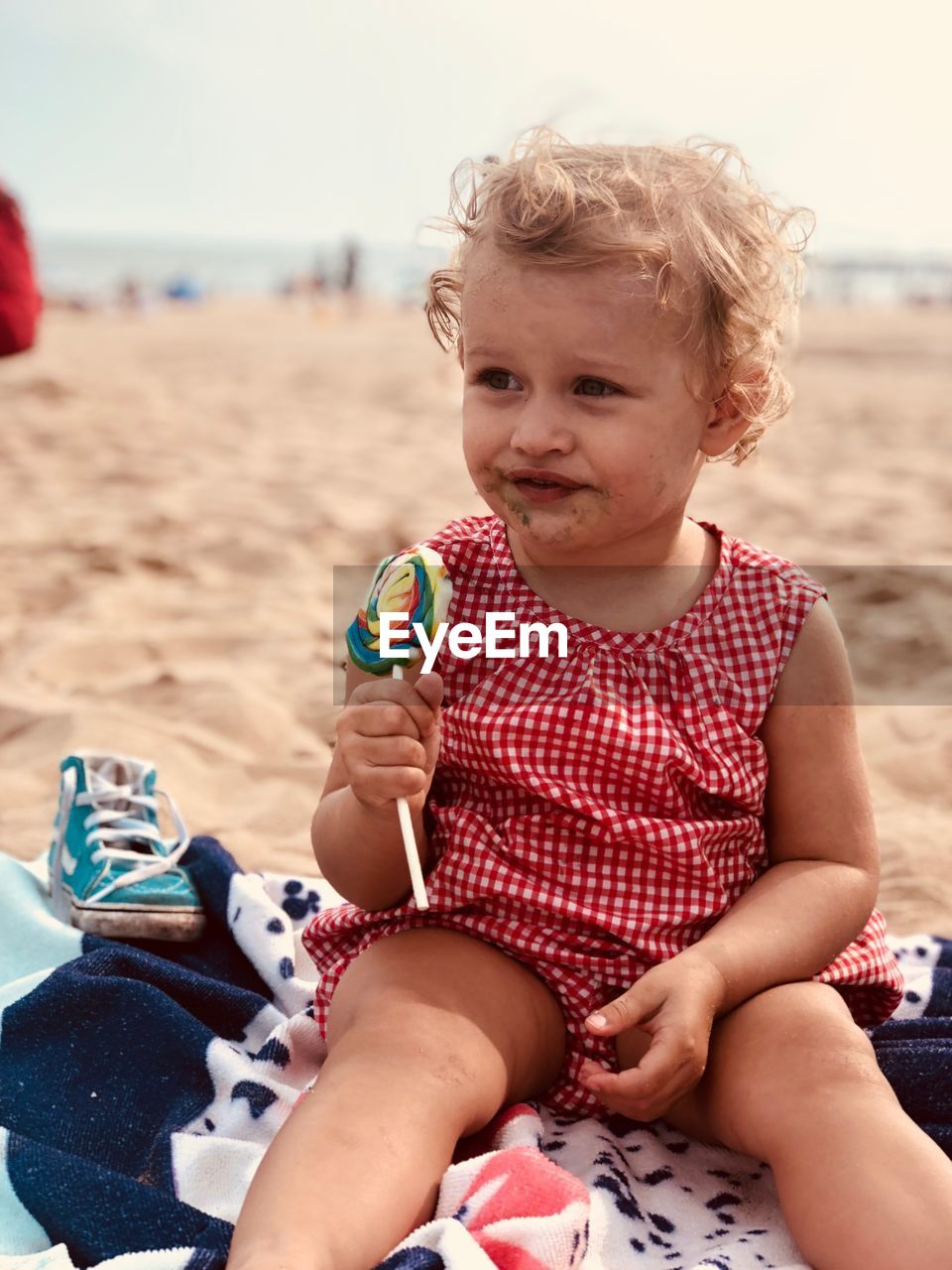 Cute girl eating lollipop while sitting at beach