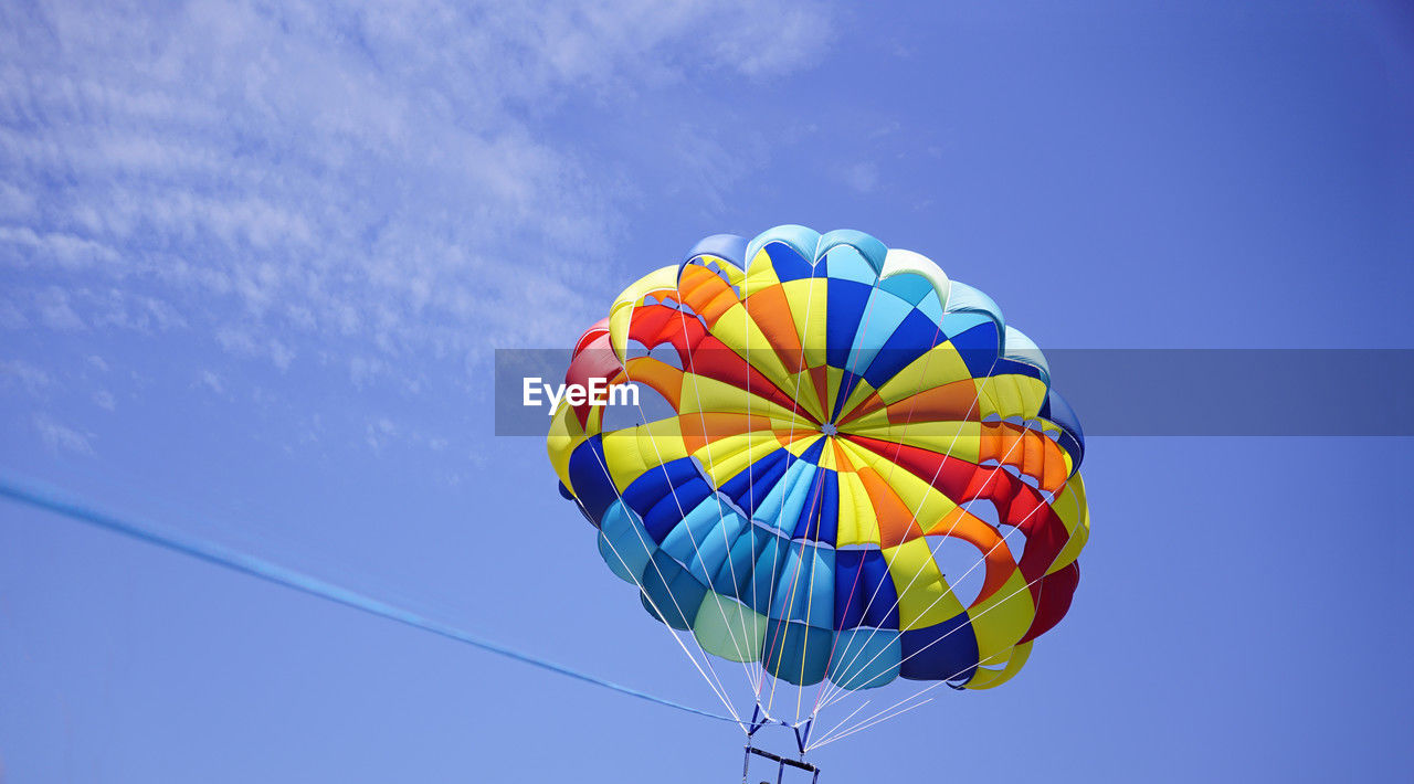 sky, parasailing, multi colored, blue, adventure, water sports, flying, mid-air, sailing, sports, parachute, low angle view, transportation, extreme sports, nature, windsports, balloon, paragliding, kite sports, toy, cloud, air vehicle, day, hot air balloon, clear sky, leisure activity, motion, vibrant color, outdoors, environment, recreation, joy, fun, holiday, wind, rope