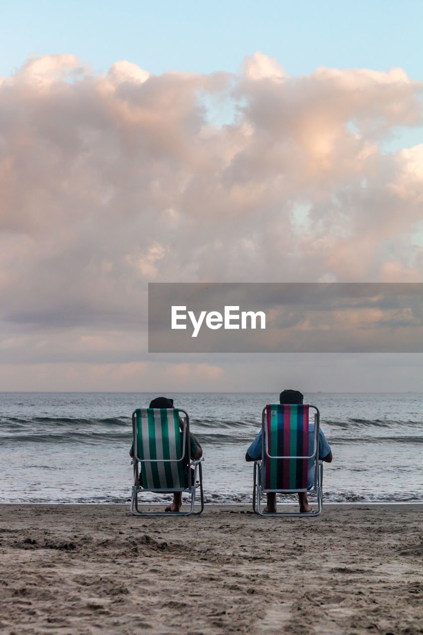 Scenic view of beach against sky. two people sitting on chairs looking at the horizon
