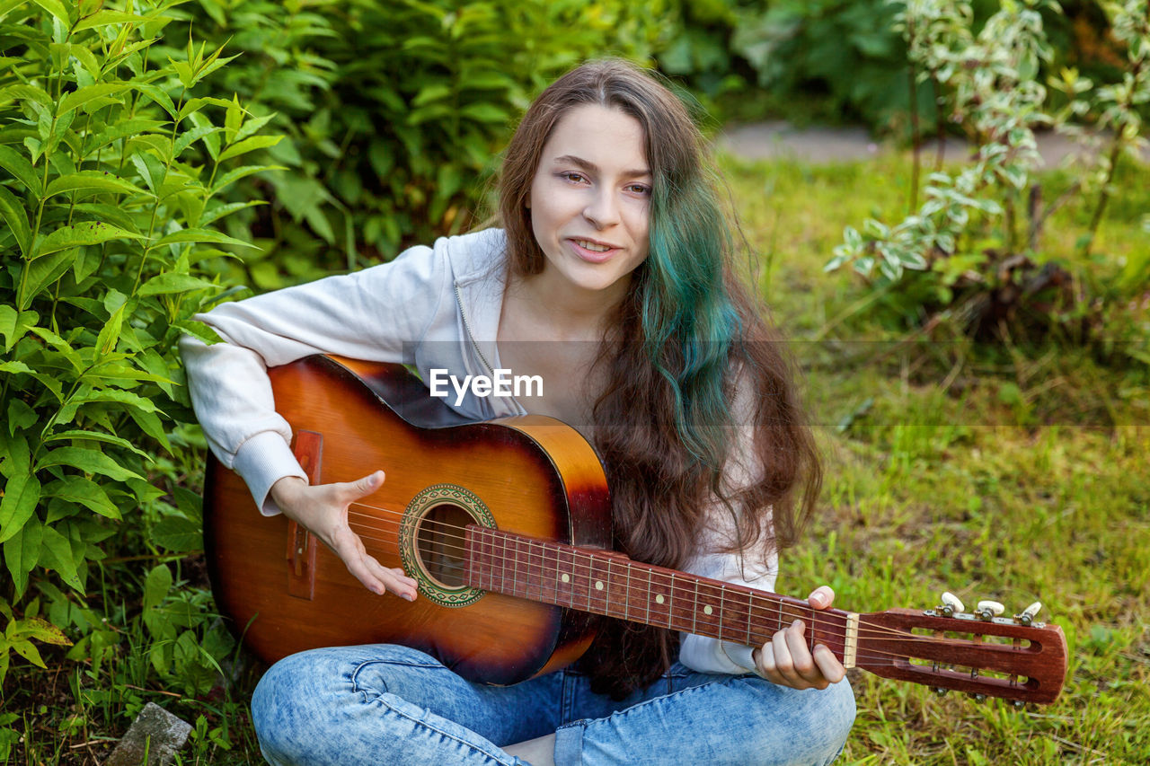 young woman playing guitar while sitting on field