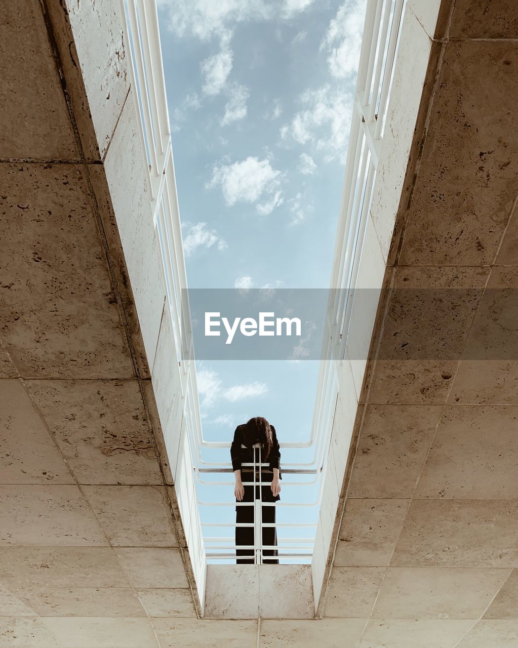 Low angle view of woman leaning on railing against sky