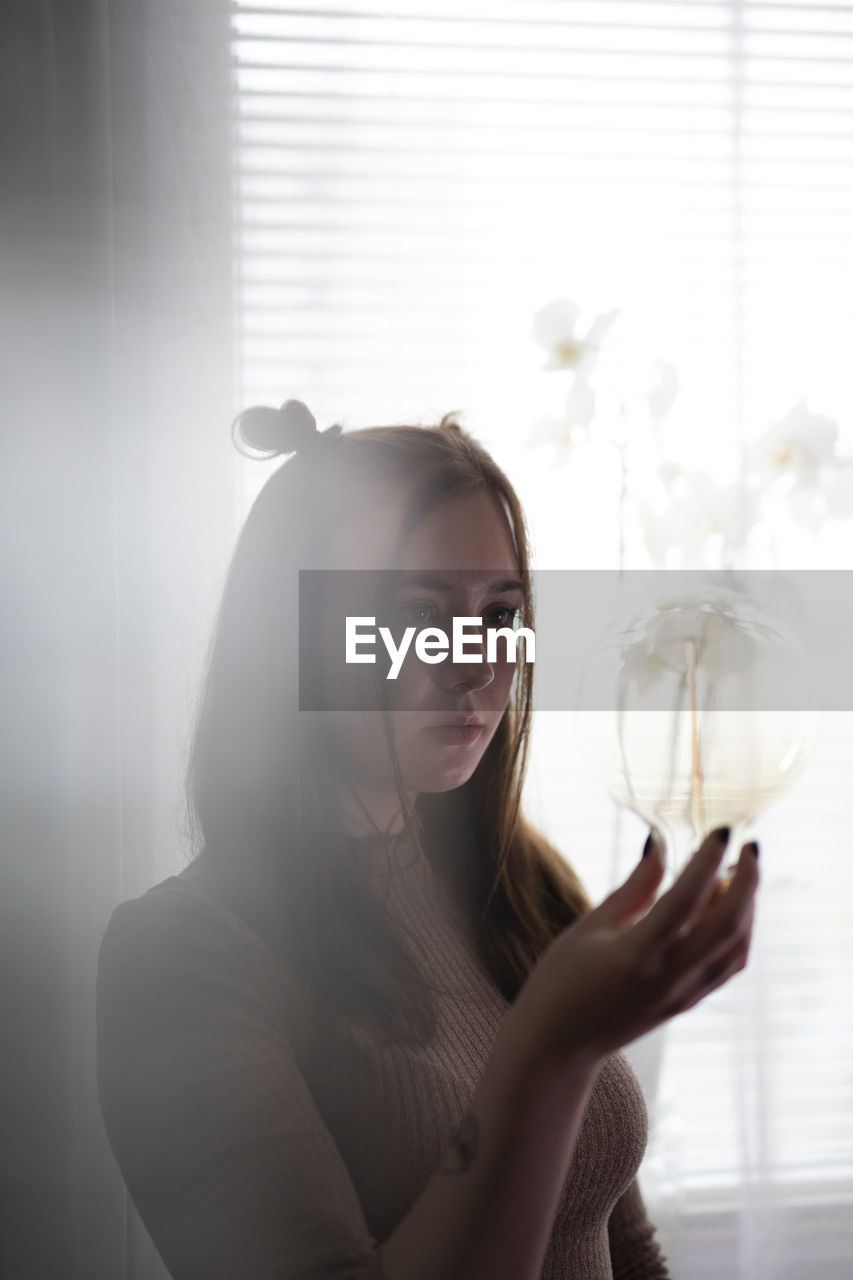 PORTRAIT OF WOMAN STANDING BY WINDOW