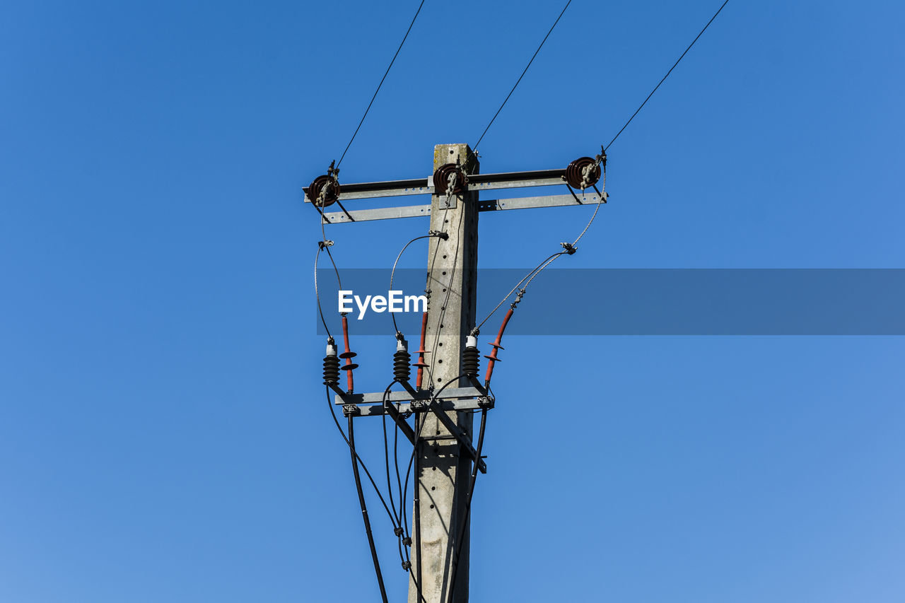 electricity, cable, technology, blue, sky, overhead power line, clear sky, power supply, power generation, electricity pylon, low angle view, power line, electrical supply, no people, mast, nature, day, transmission tower, street light, telephone pole, lighting, communication, telephone line, outdoors, public utility, antenna, copy space, sunny, line, wind, lighting equipment