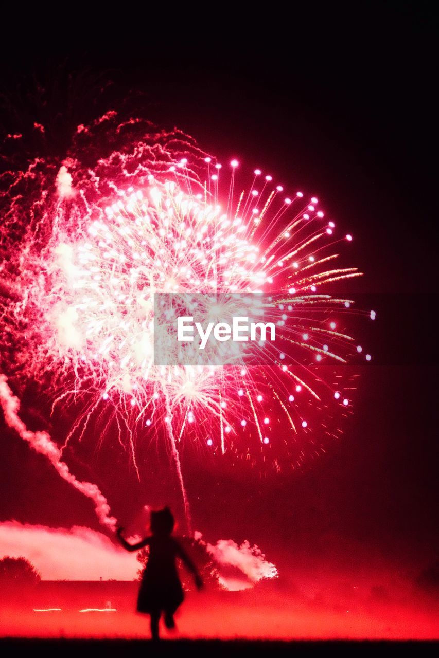 Full length of silhouette girl running against firework display at night