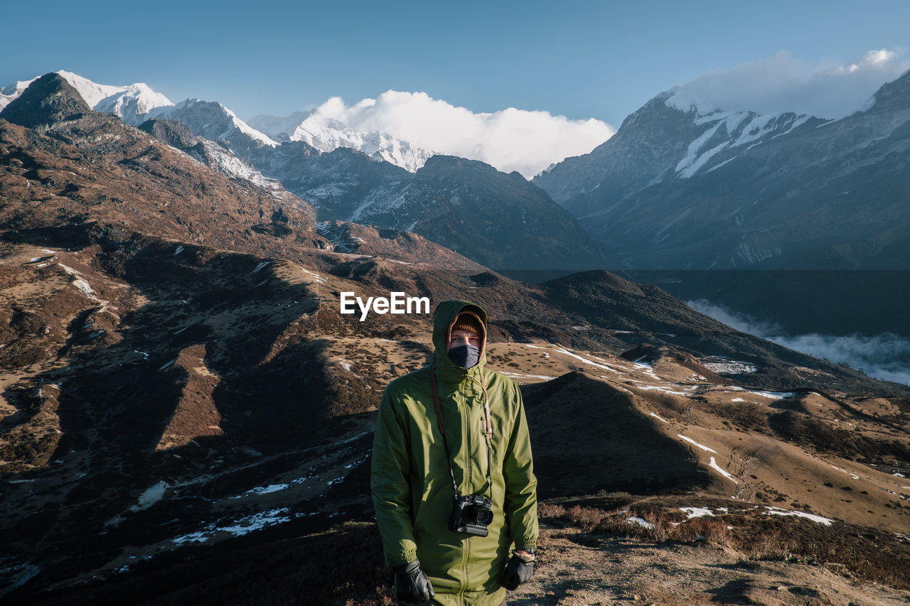 MAN STANDING BY MOUNTAINS AGAINST SKY