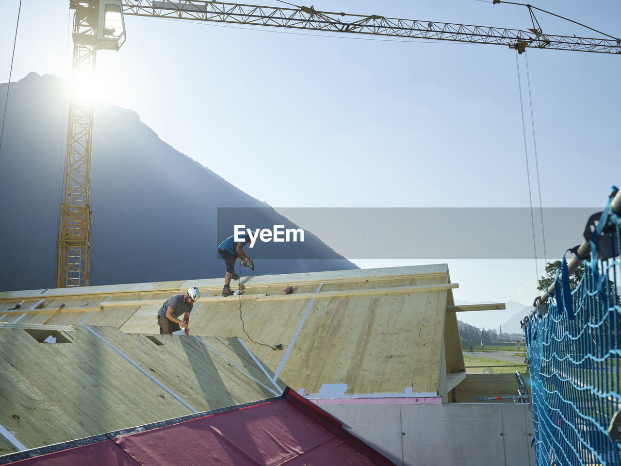 Coworkers installing wooden roof on sunny day