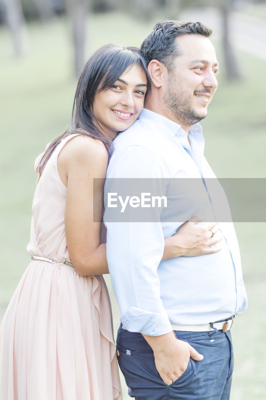 PORTRAIT OF A SMILING YOUNG COUPLE STANDING OUTDOORS