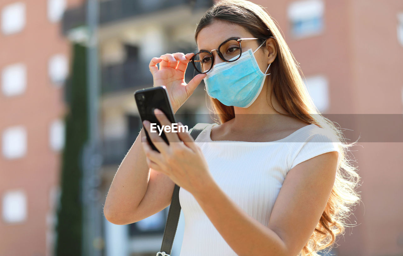 Woman wearing mask using phone while standing outdoors