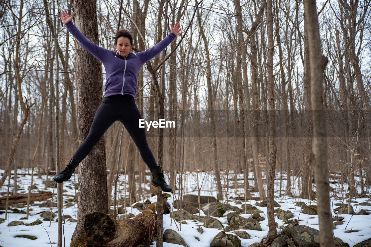 Full length of woman jumping in snow covered woods