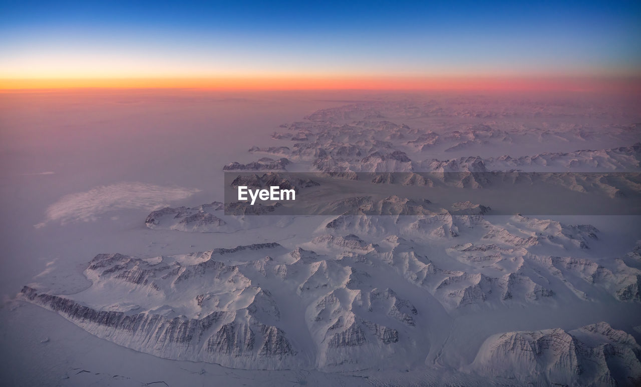 Aerial view of snowcapped landscape greenland against sky during sunset