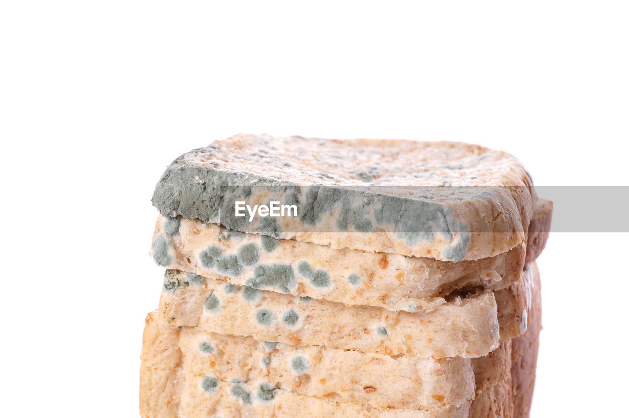 Close-up of stacked breads with fungal mold against white background