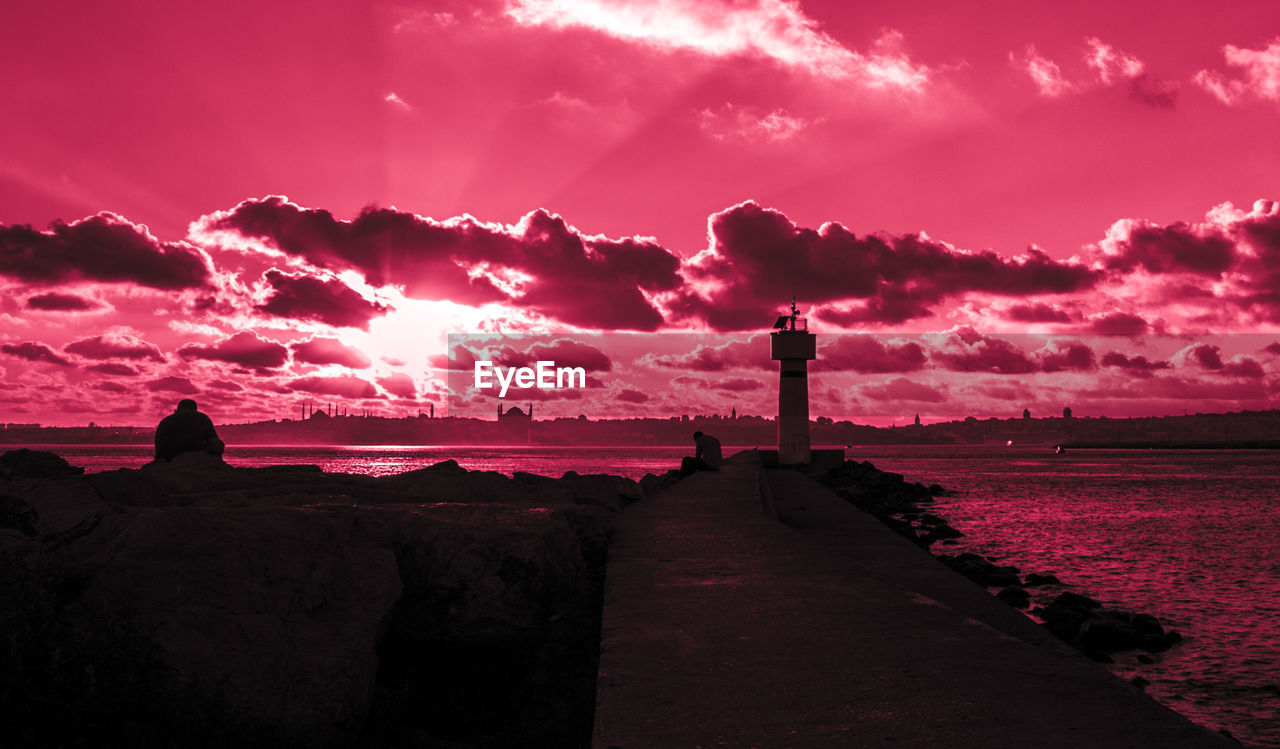 Lighthouse against sea and scenic sky at sunset