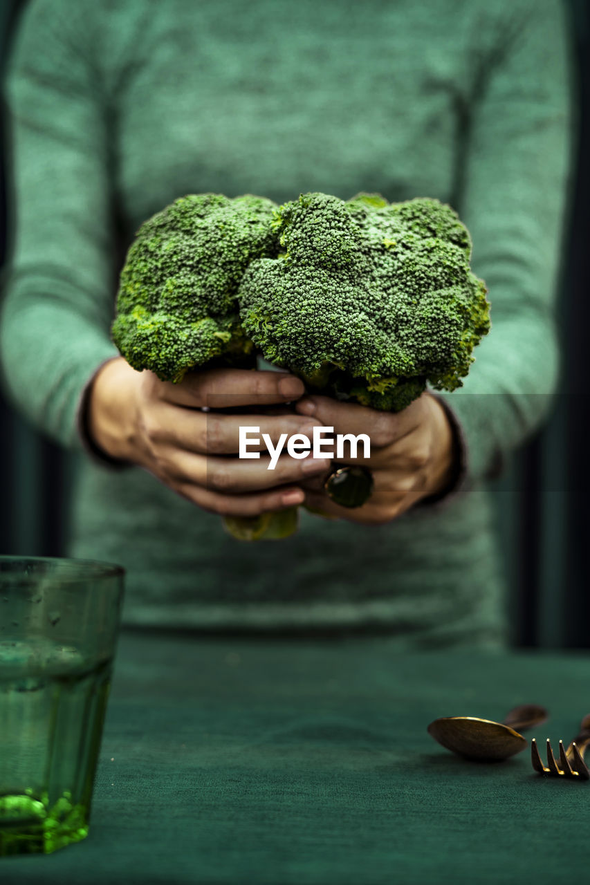 Midsection of woman standing with broccoli and spoon, fork, glass kept on table