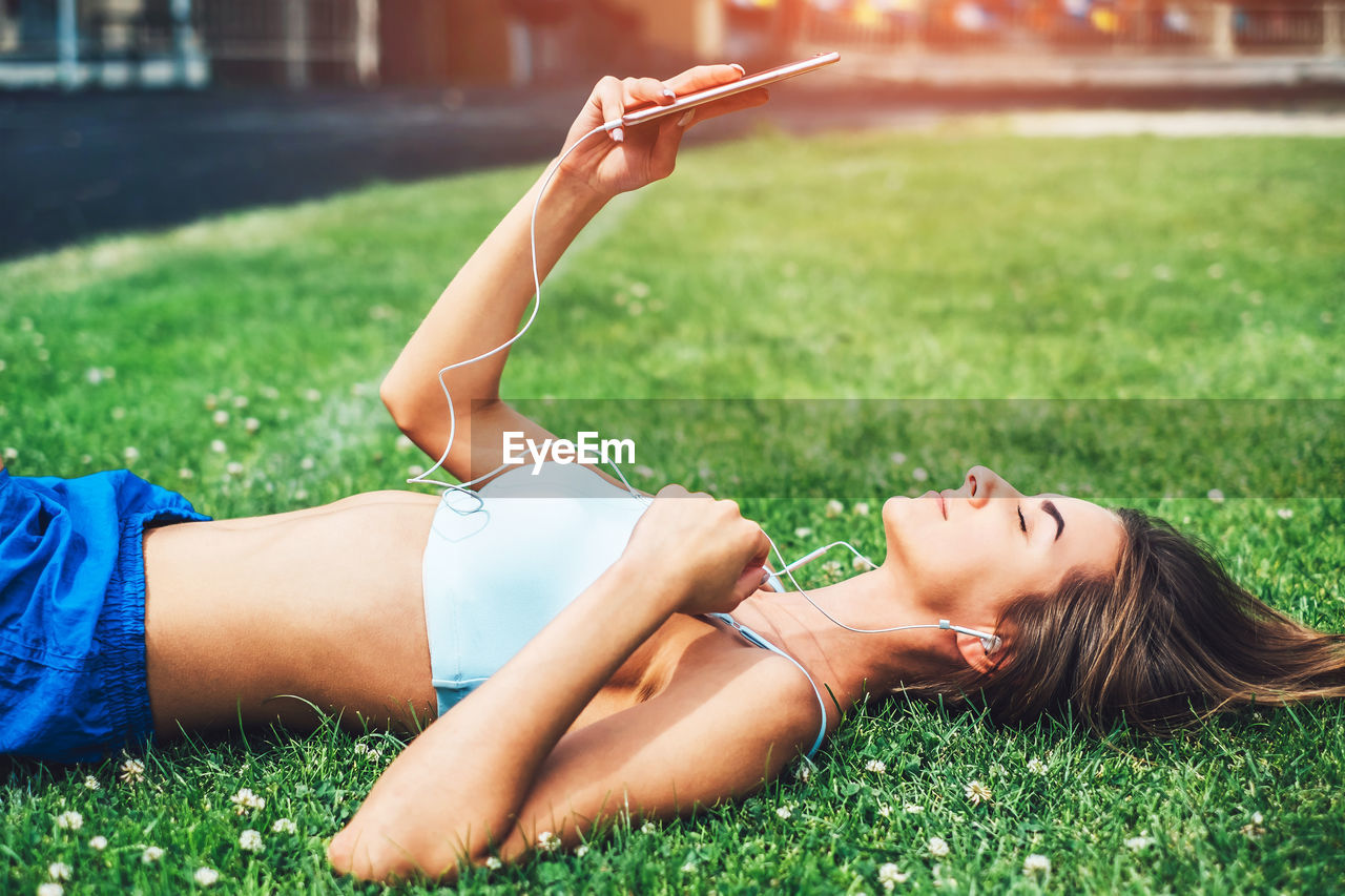 Side view of young woman listening to music while lying on field