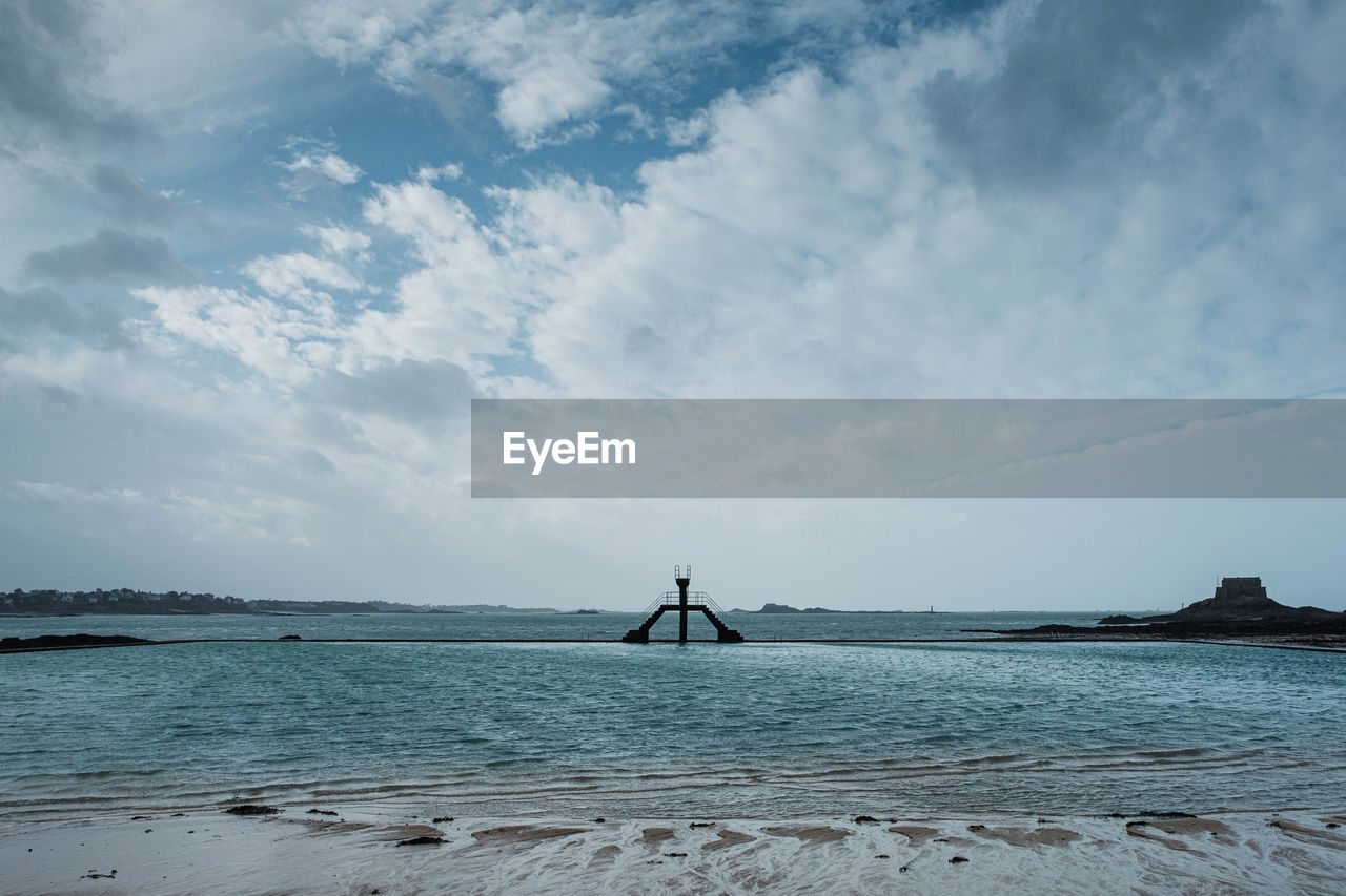 Scenic view of sea against sky. swimming pool on natural beach with jumping tower.