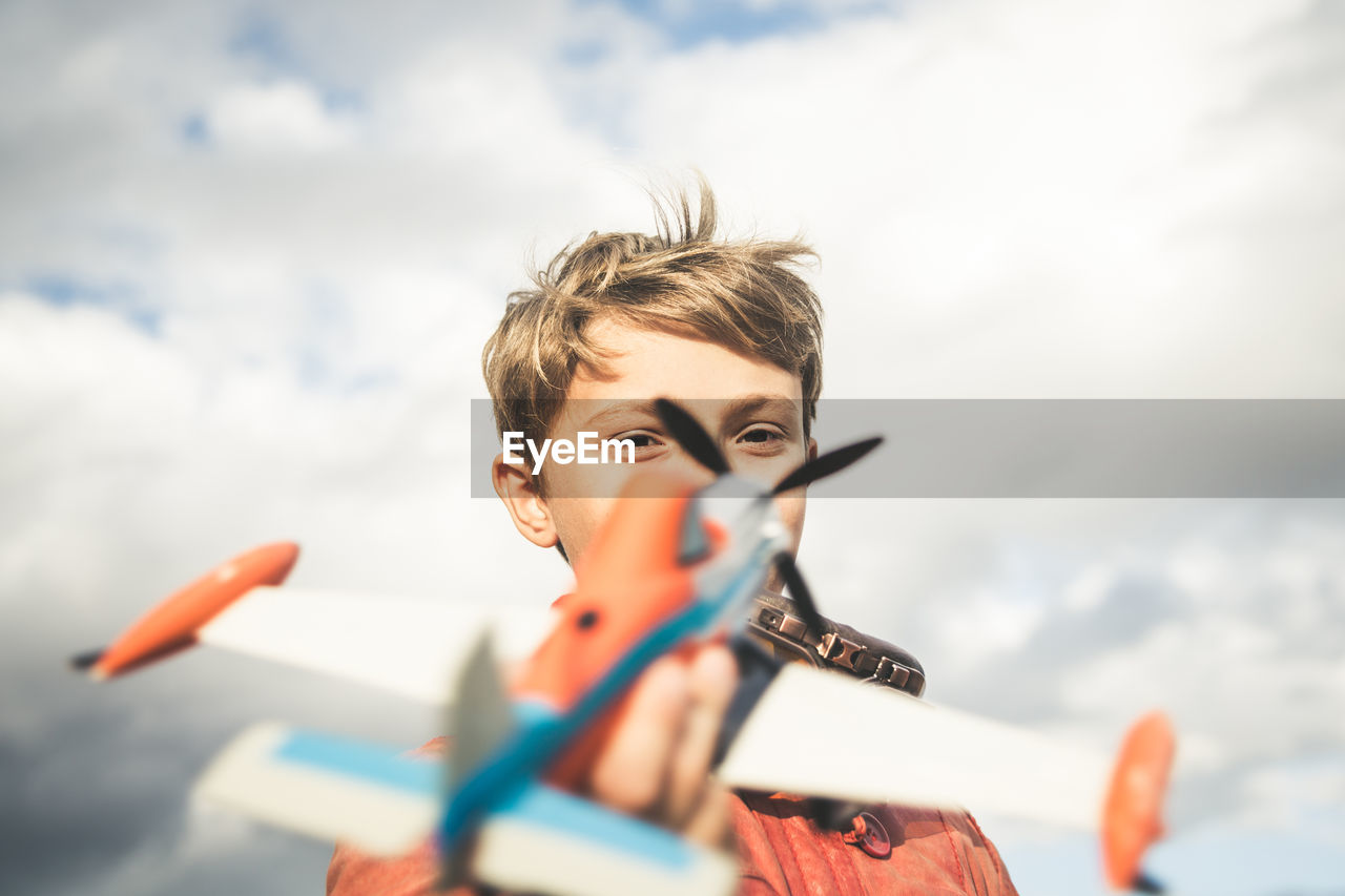 Portrait of boy playing with toy airplane against sky