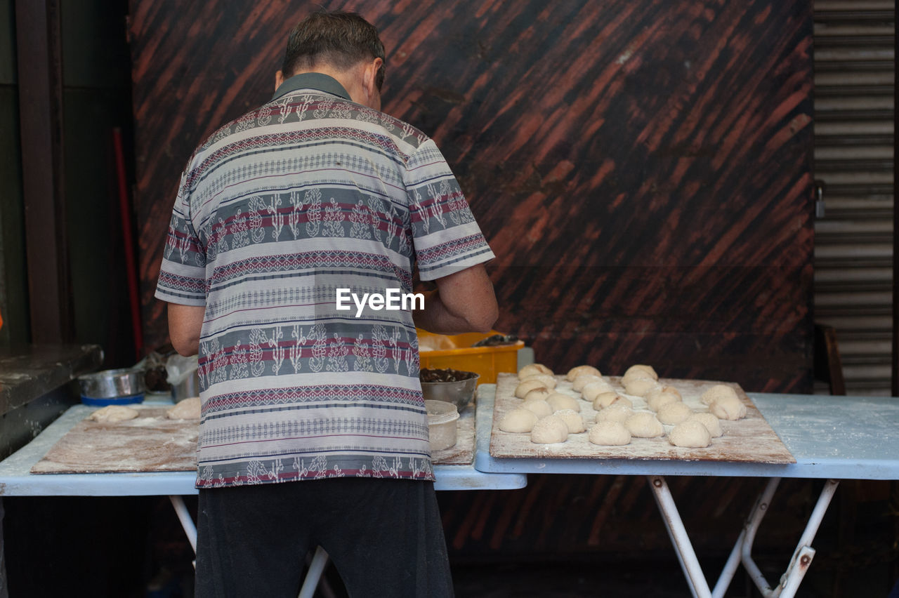 REAR VIEW OF MAN PREPARING FOOD ON TABLE