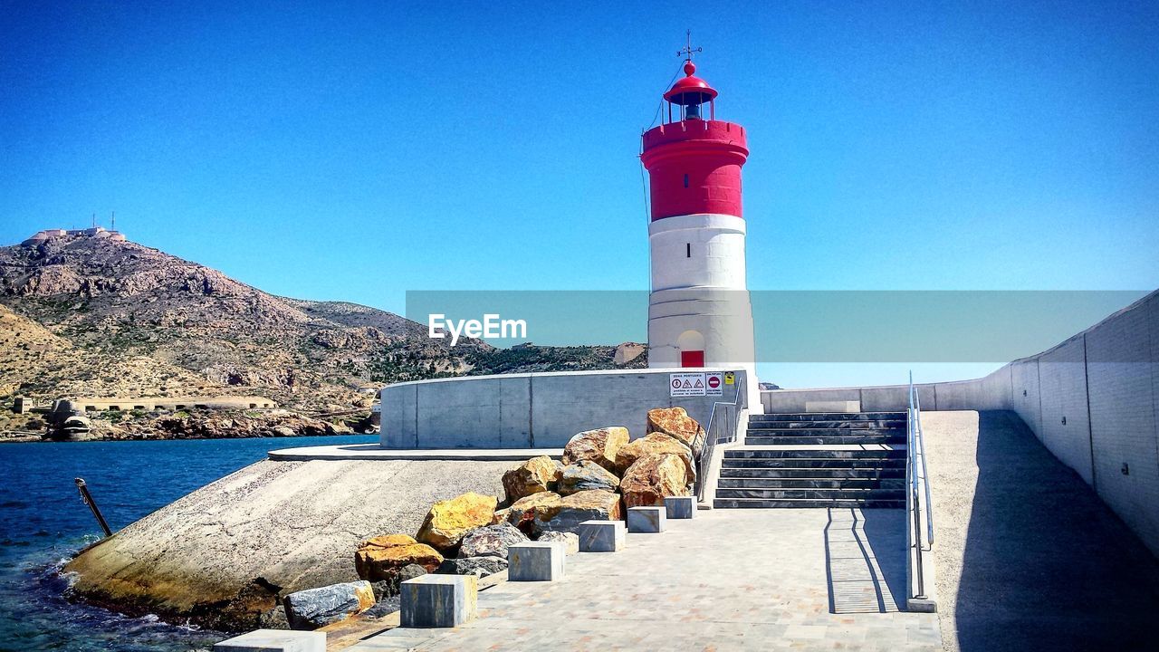 LIGHTHOUSE BY SEA AGAINST BLUE SKY