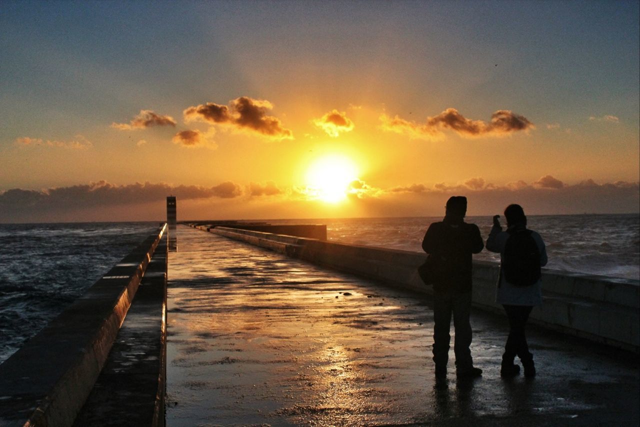 Silhouette friends standing on pier over during sunset