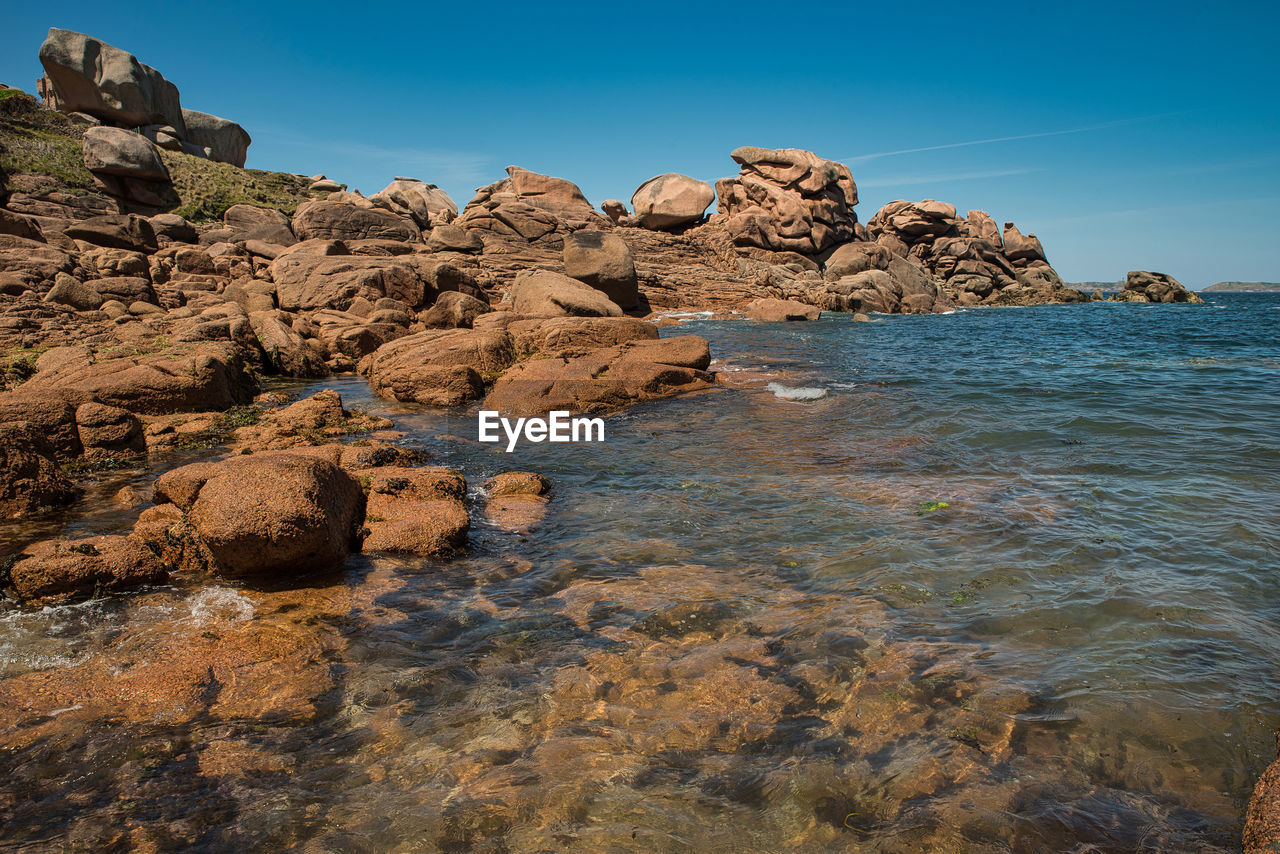 Rocks in sea against clear blue sky