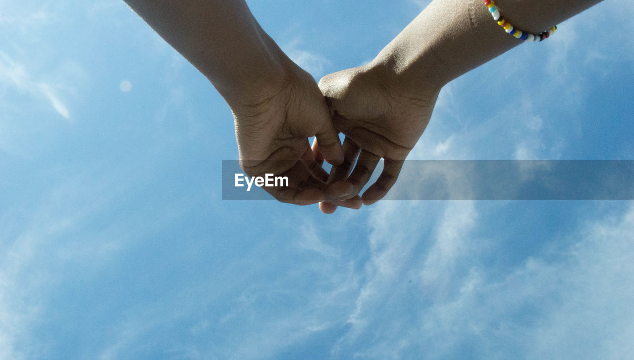 Low angle view of hands against blue sky