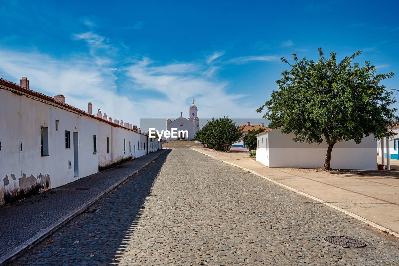 Empty road by buildings against blue sky