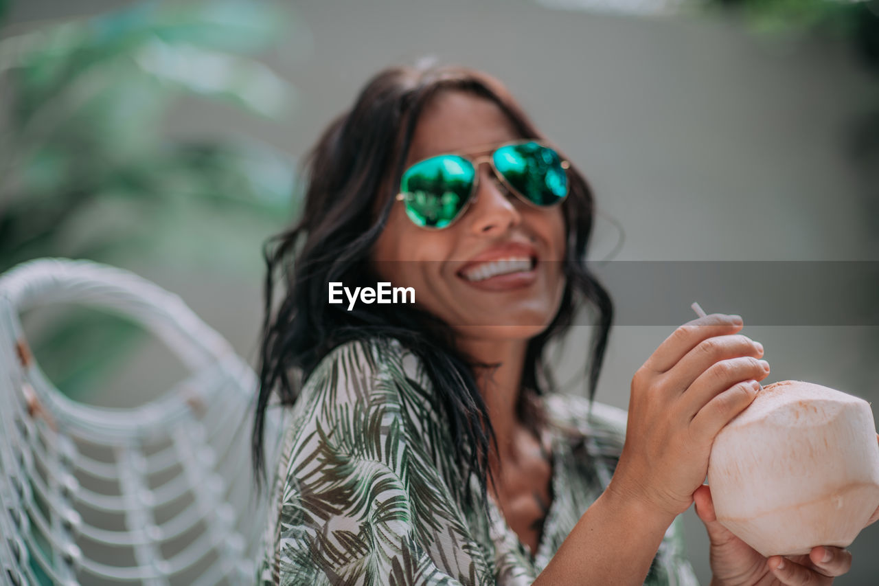 Portrait of a smiling young woman holding sunglasses