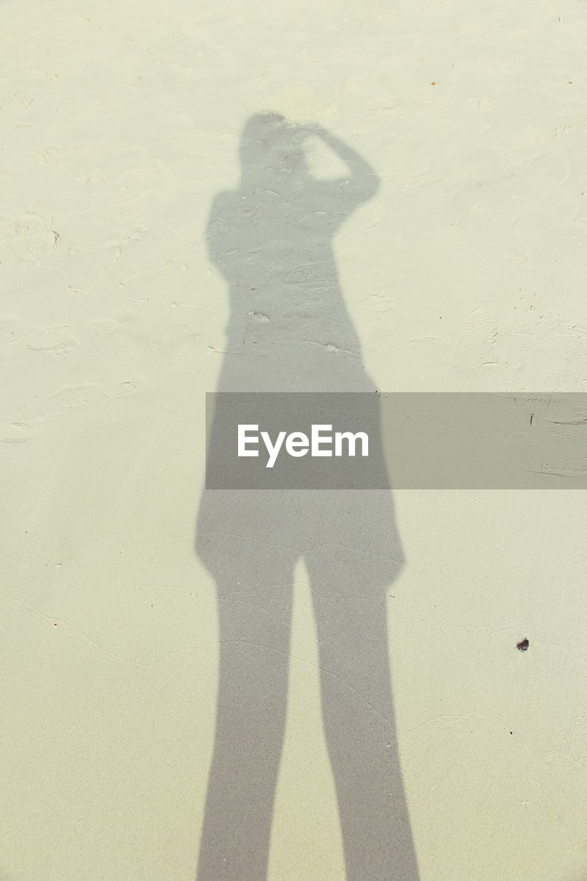 SHADOW OF MAN STANDING ON SAND AT BEACH