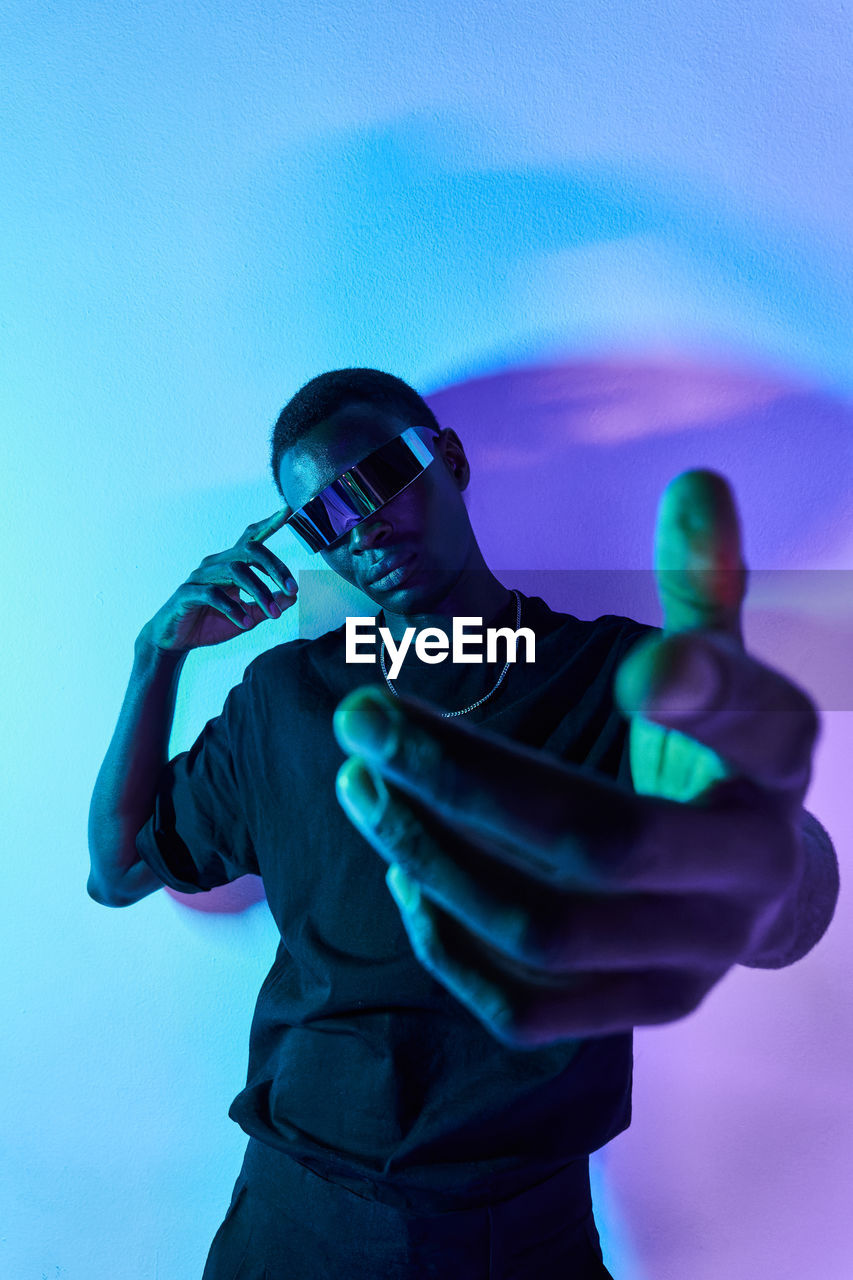 Concentrated young african american male millennial in casual clothes and vr glasses reaching out hand toward camera against colorful background