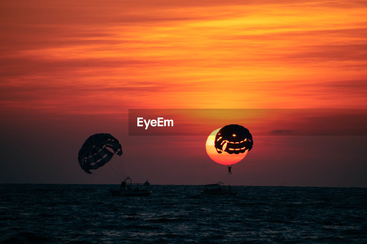 low angle view of silhouette woman with balloons against orange sky