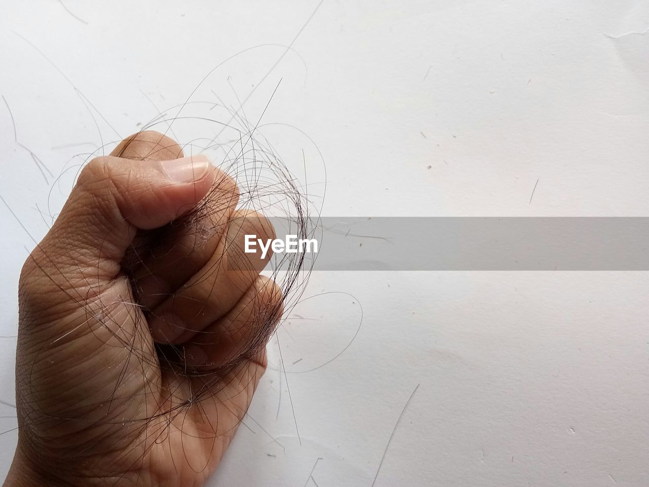 Close-up of hand holding hair against white wall