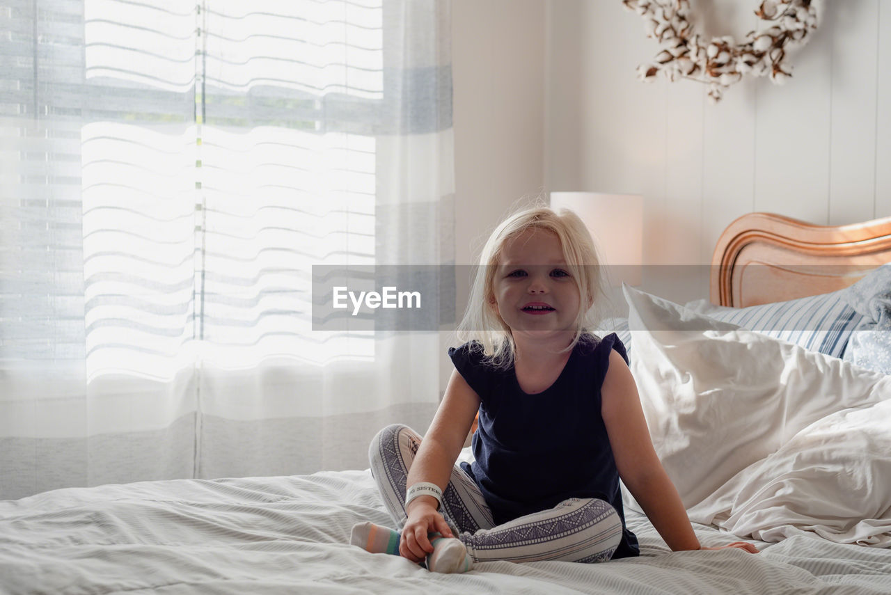 Full length portrait of girl sitting on bed at home